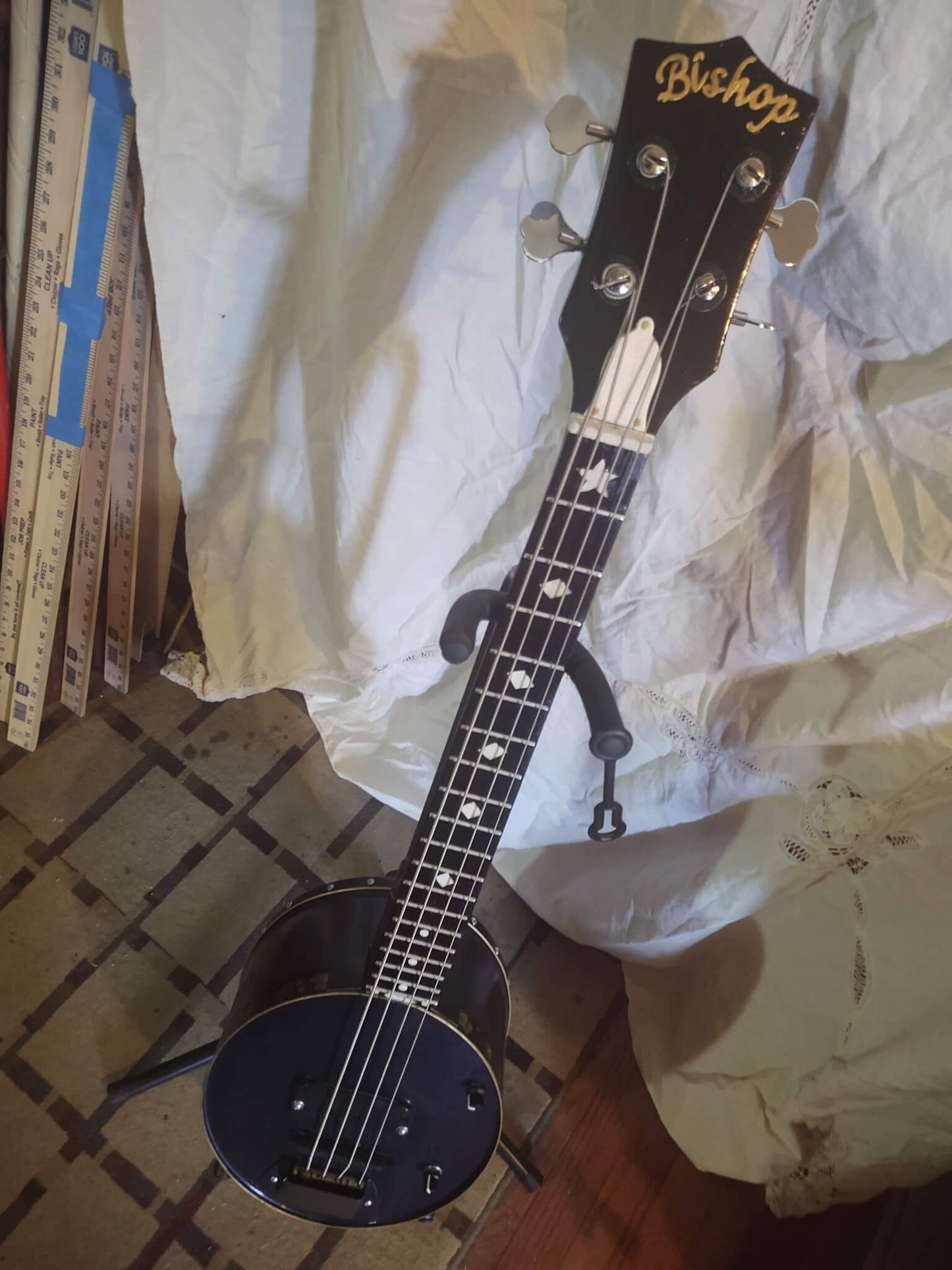 A custom Bishop Blueridge Tinjo Bass with a purple-to-blue shifting finish, 4-string setup, dual pickups, and a resonator-style metal body, displayed on a stand against a white fabric backdrop.
